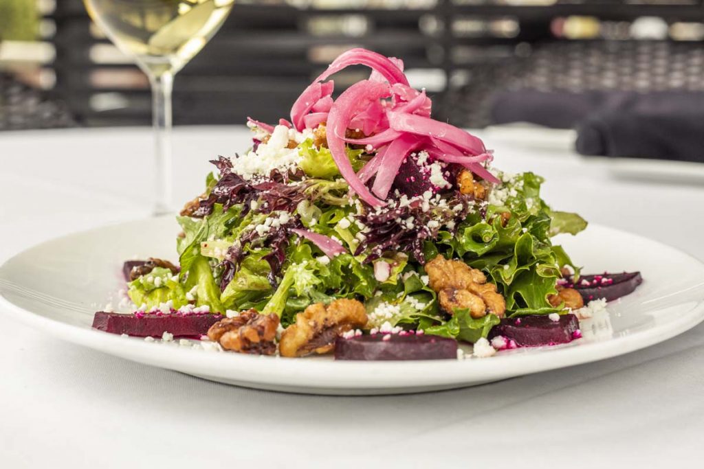 Tucci’s salad topped with pickled red onion with white wine in background