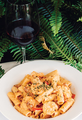 Plated dish of rigatoni with shrimp and glass of red wine.