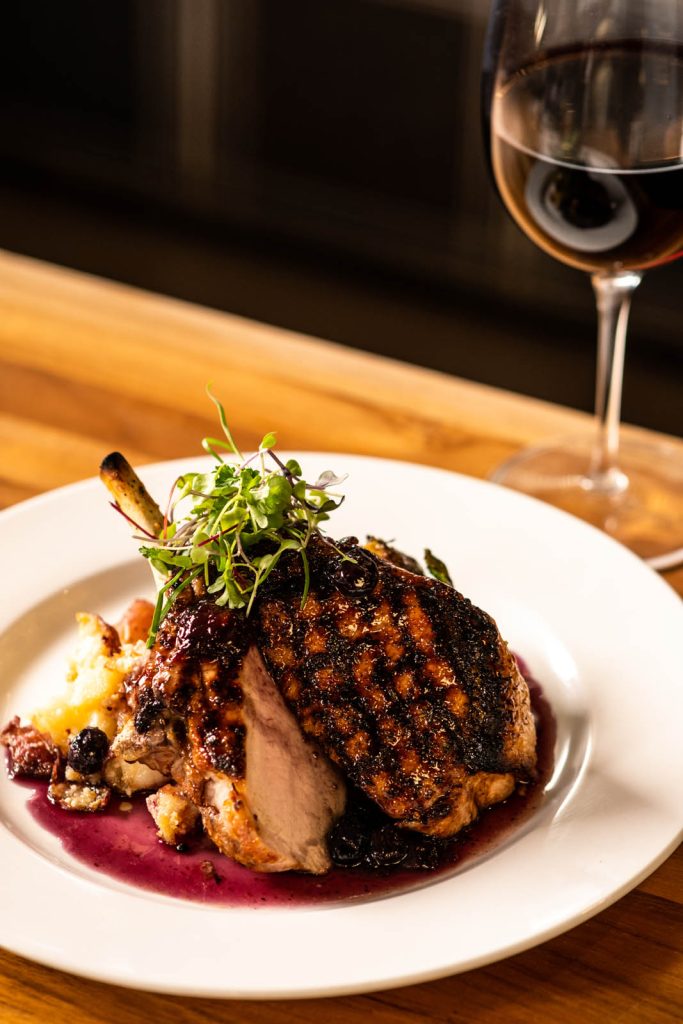 Seared Berkshire Pork Chop with glass of red wine on table at Tucci's in Carmel City Center, Indiana.
